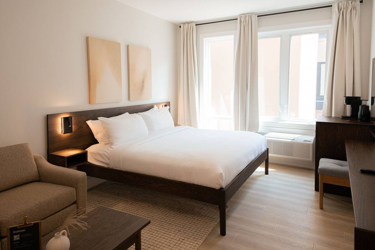 A hotel room with a bed, a sofa, a desk, and a window with curtains.