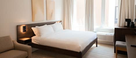 A hotel room with a bed, a sofa, a desk, and a window with curtains.