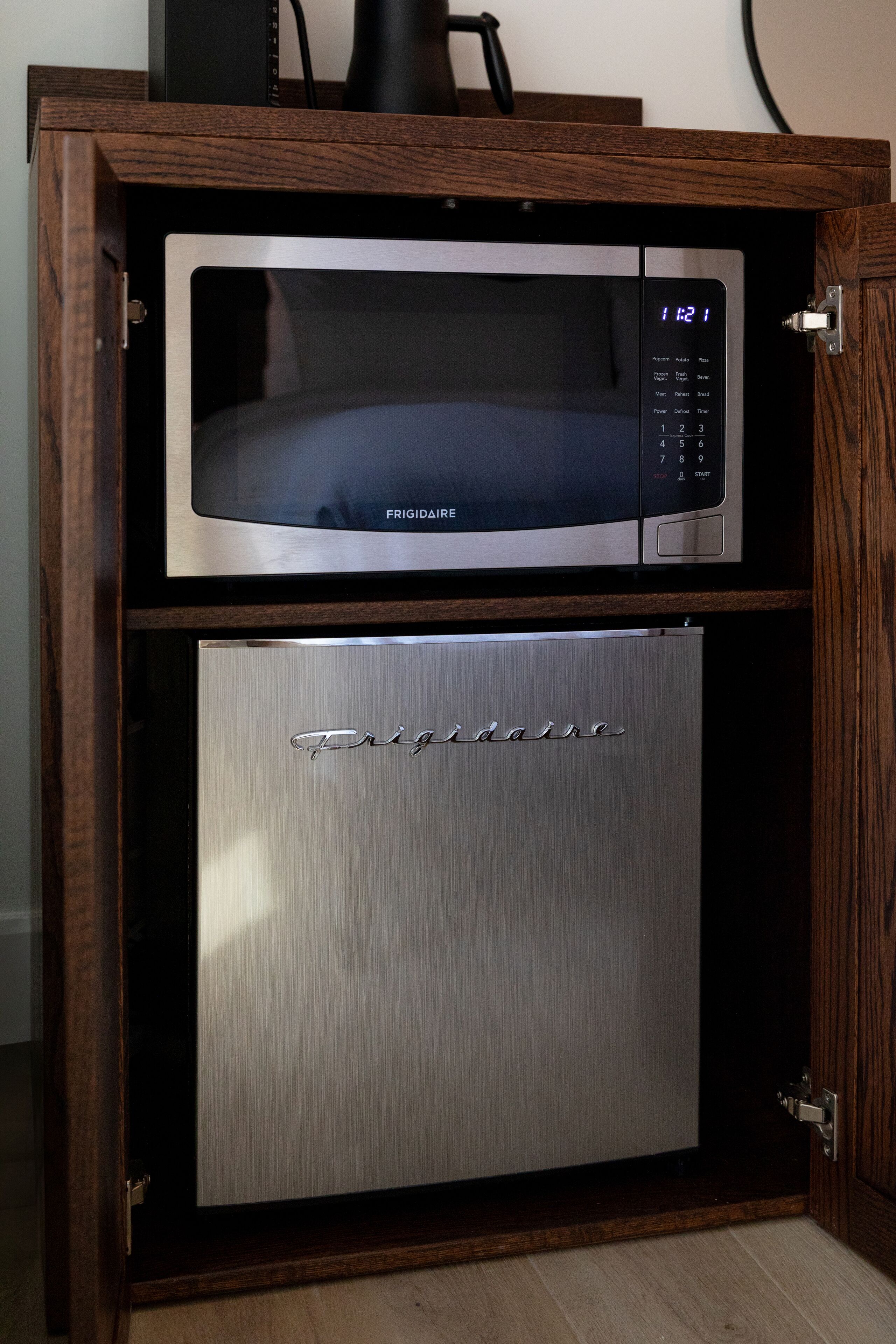 A compact kitchen with a built-in microwave and a stainless steel mini-fridge.