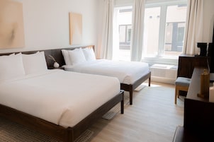 A hotel room with two beds, a desk, and a view of the outside.