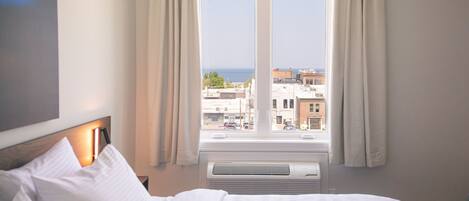 A hotel room with a large bed, a view of the city through a window, and a wall-mounted air conditioning unit.