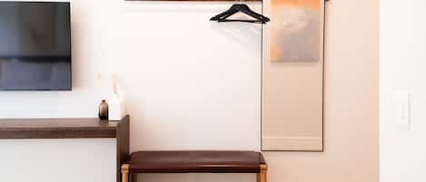 A room with a wooden bench, a flat-screen TV, a framed artwork, and a wooden shelf.