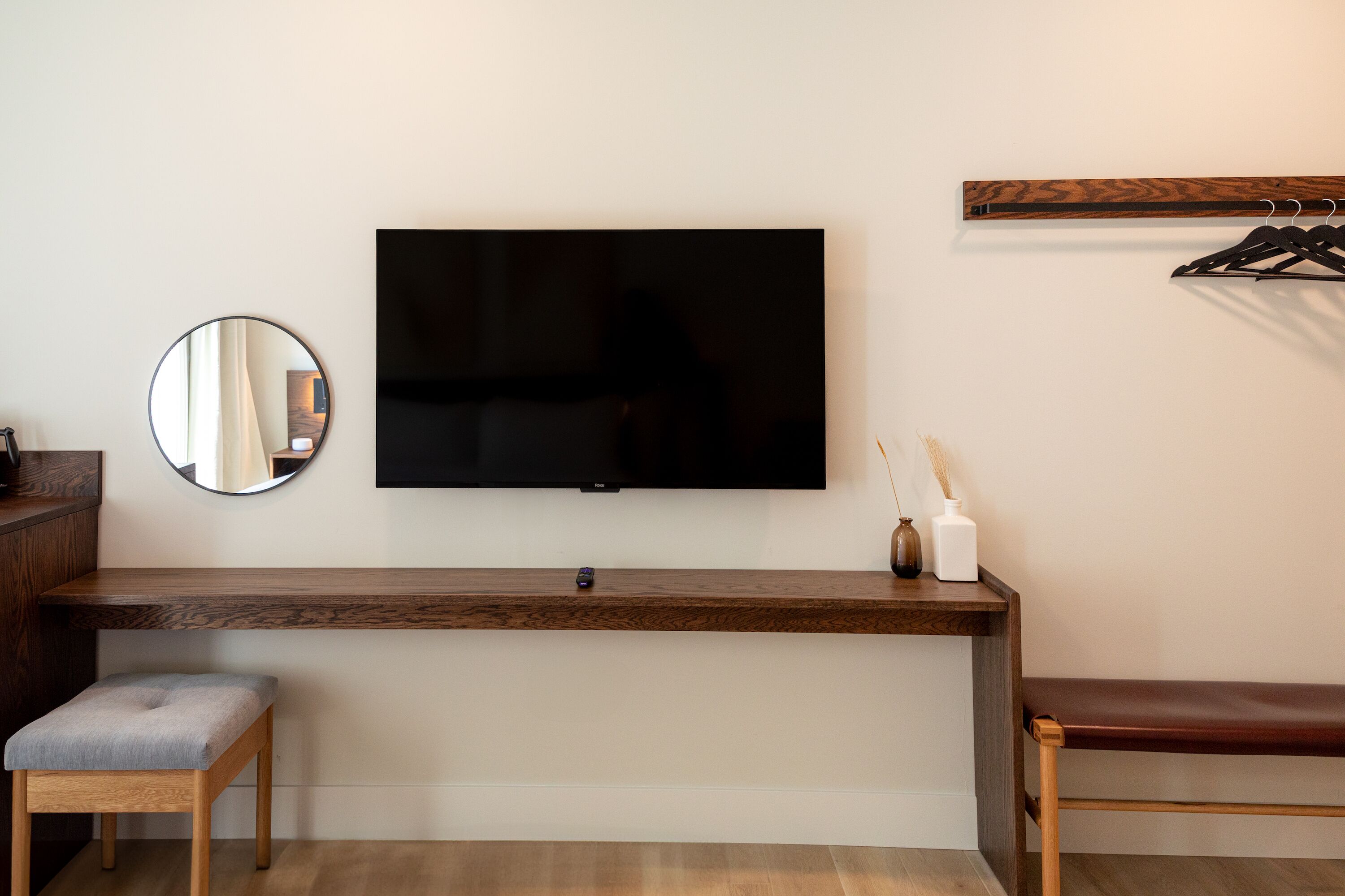 Una habitación moderna con una televisión de pantalla plana en la pared, un banco de madera, un taburete pequeño y un espejo.