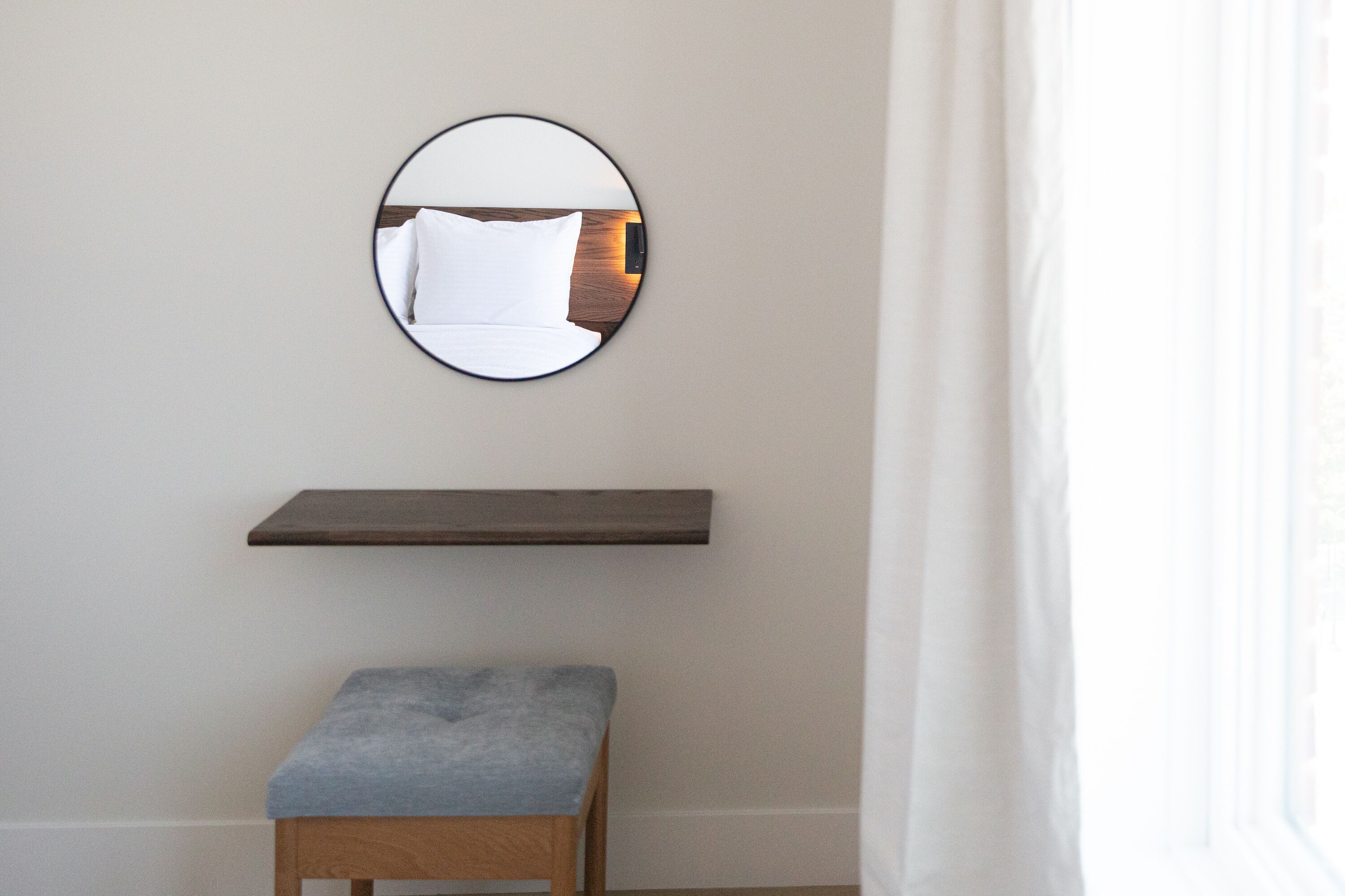 A room with a round mirror on the wall, a wooden bench, and a shelf below the mirror.