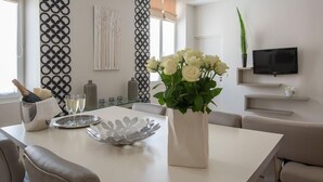 A modern dining area with a white table, a vase of white flowers, a metal charger, and a bottle of champagne. - O Carré Croisette (Cannes)