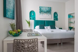 A modern hotel room with a bed, a dining table, and chairs. There are two wall-mounted shelves with decorative items and a painting above the bed. - O Carré Croisette (Cannes)