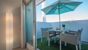 A balcony with a table and chairs, a blue umbrella, and a small garden area. - O Carré Croisette (Cannes)