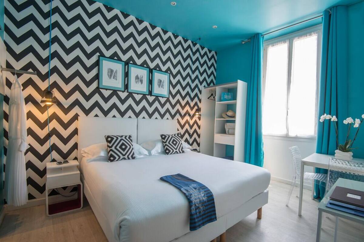 A modern bedroom with a white bed, a zigzag patterned wall, and a teal accent wall.