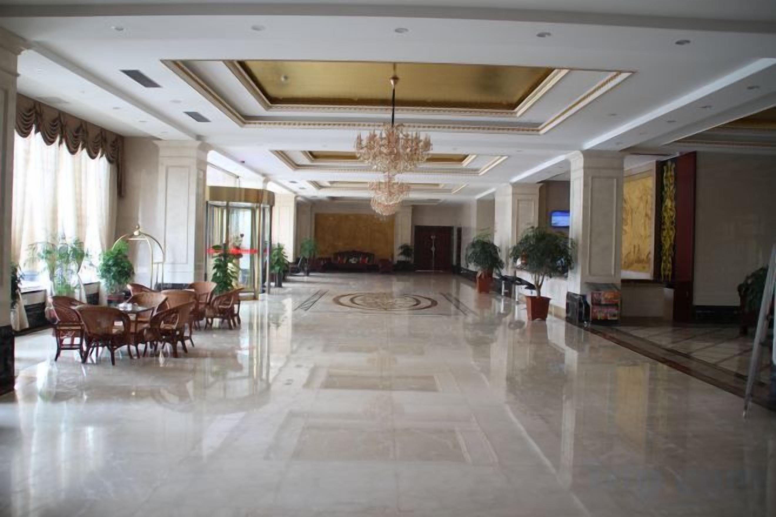 A spacious lobby with a chandelier, seating area, and potted plants.