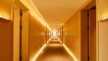 A hotel corridor with doors marked with room numbers, a patterned floor, and a ceiling light.