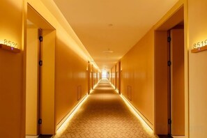 Un pasillo de hotel con puertas numeradas, suelo estampado e iluminación en el techo.