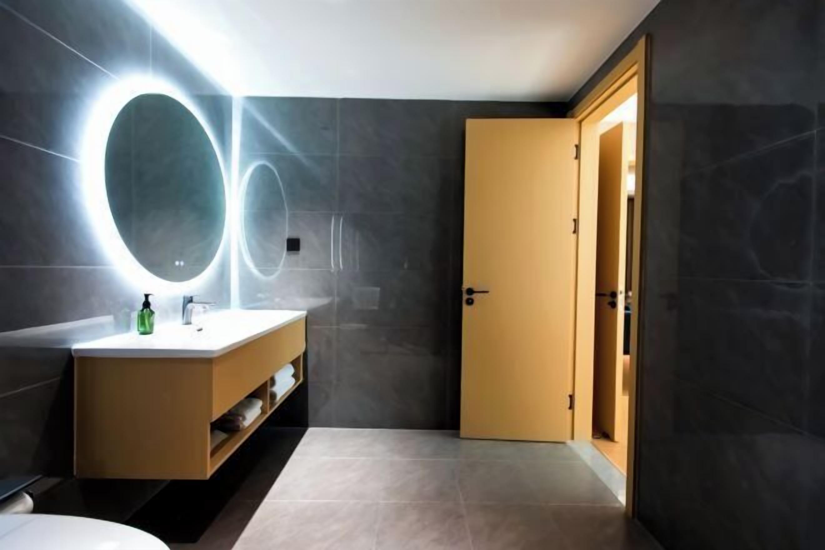 A modern bathroom with a vanity, mirror, and a door leading to another room.