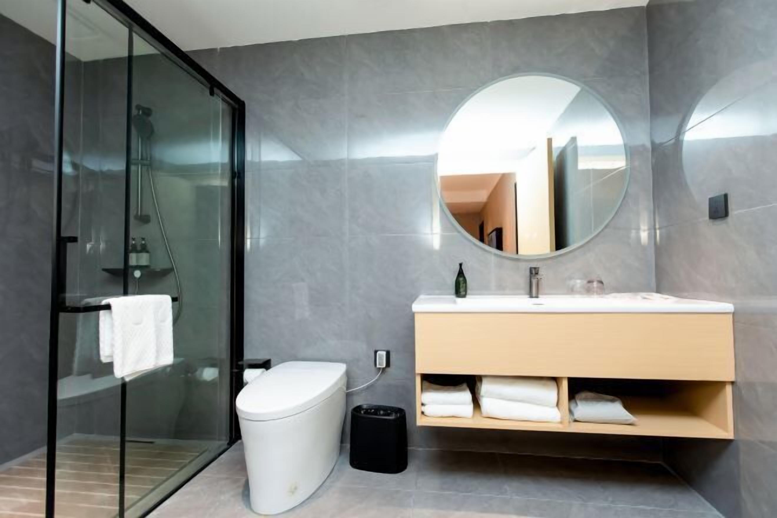 Une salle de bain moderne avec une douche à parois de verre, des toilettes, un lavabo avec un miroir et une poubelle.