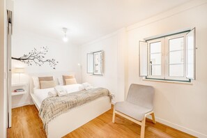 Een slaapkamer met een bed, nachtkastjes, een stoel en een raam met gordijnen.
