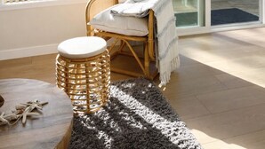 Ein gemütliches Zimmer mit einem Korbstuhl, einem runden Tisch und Seeblick durch große Fenster.