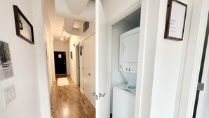 A hallway with wooden flooring, white walls, and a door leading to a laundry room with a washing machine.
