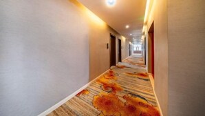 A hotel corridor with a carpeted floor, doors on both sides, and a ceiling light. - Hongxin Hotel (Ulan)