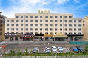 A multi-story hotel with a central entrance, parking lot, and several ground-level commercial establishments. - Hongxin Hotel (Ulan)