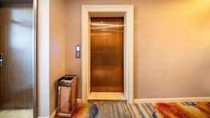 An elevator with a metallic interior, a wall-mounted control panel, and a carpeted floor. - Hongxin Hotel (Ulan)