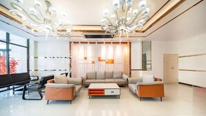 A modern hotel lobby with a seating area, a large chandelier, and a large window. - Hongxin Hotel (Ulan)