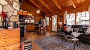 Ein gemütliches Blockhaus-Interieur mit Steinwand, Holzbalkendecke, Essbereich, Wohnzimmer mit Sofa und Küche.