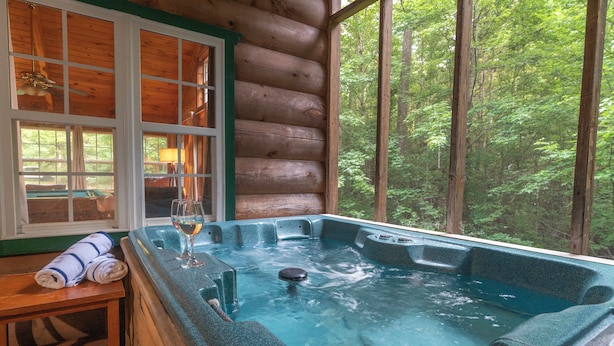 Eine Holzhütte mit Whirlpool, einem Fenster mit Blick auf den Wald und einer Bank mit Handtüchern.