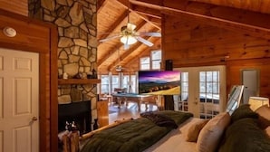 Ein gemütliches Blockhaushaus-Interieur mit Kamin aus Stein, einem großen Fernseher und einer Holzbalkendecke.