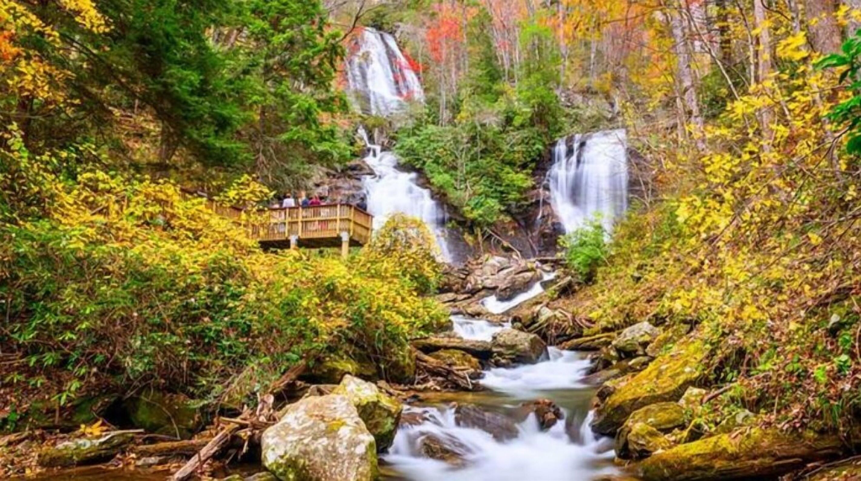 A waterfall surrounded by autumn foliage, with a wooden viewing platform.