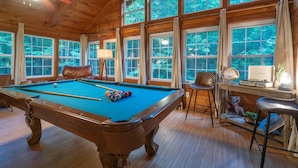 Ein Zimmer aus Holz mit Poolbillard, großen Fenstern und einem Deckenventilator.