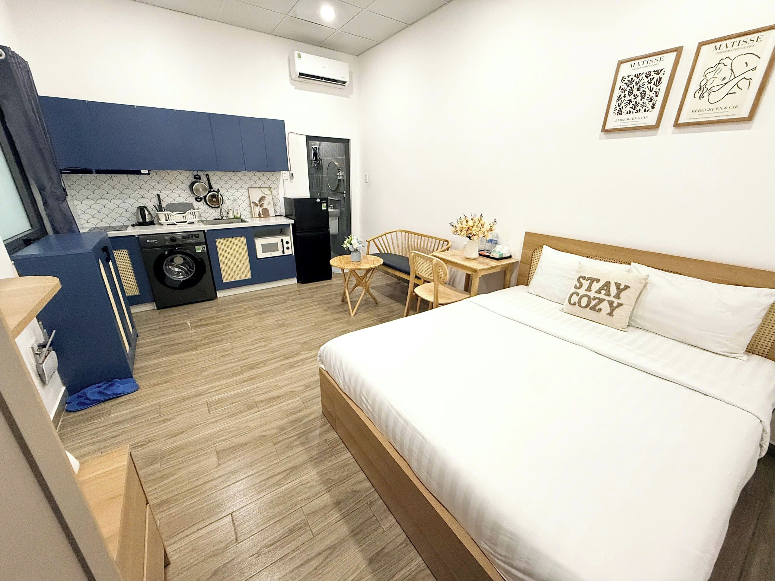 Ein kompaktes Hotelzimmer mit einem Bett, einer kleinen Küchenzeile, einem Essbereich und einer Waschmaschine.