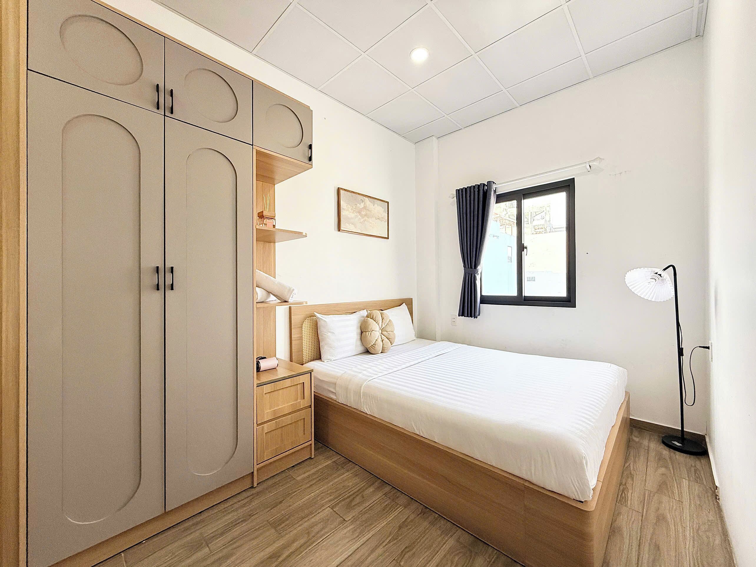 Une chambre à coucher comprenant un lit, une table de chevet, une armoire et une fenêtre avec des rideaux.