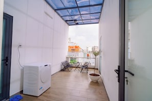 Un lavadero con lavadora, sillas, una planta en maceta y una puerta de cristal que da a un balcón exterior.