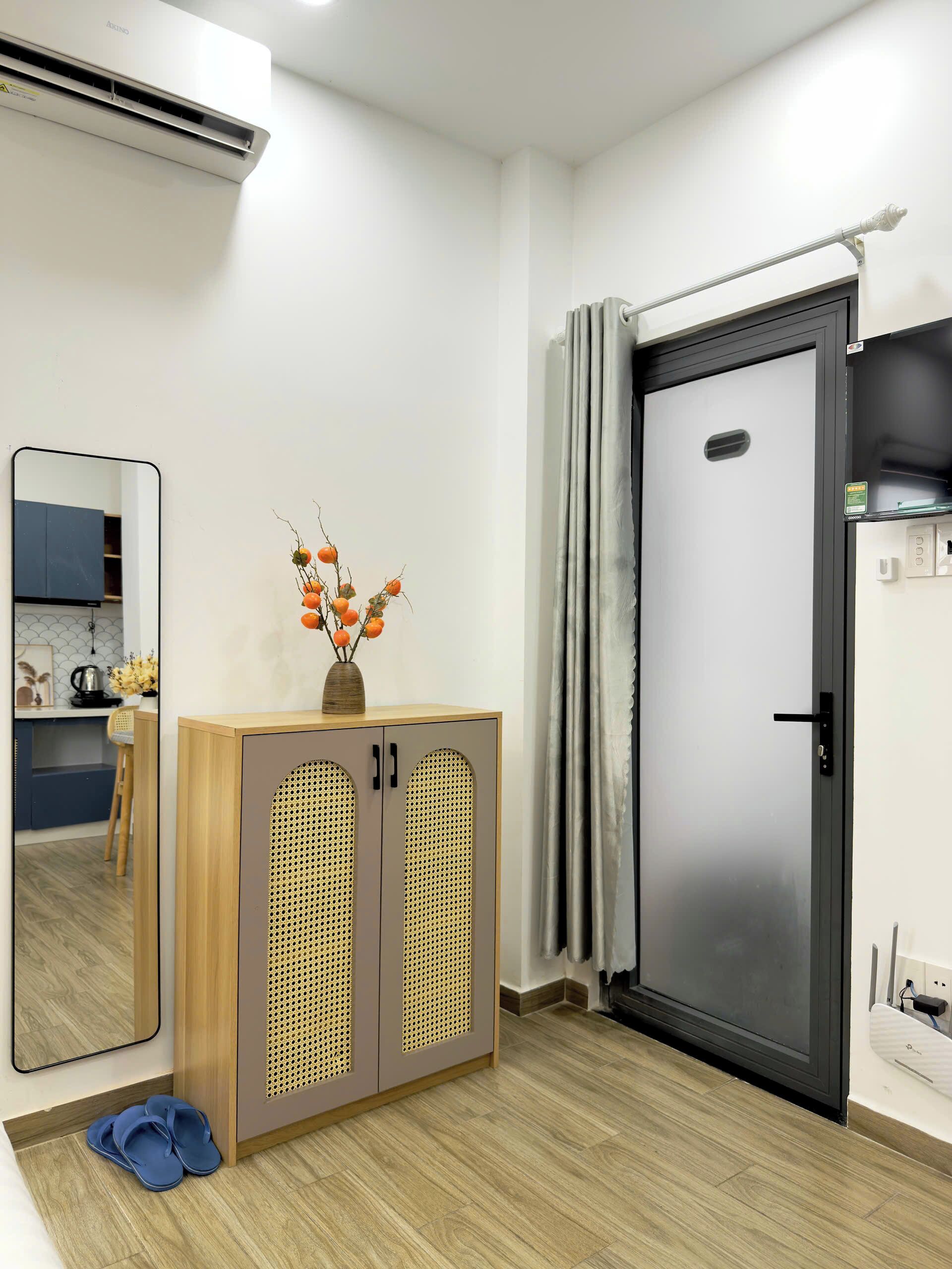 Une chambre moderne avec un meuble en bois, un miroir, une porte et une petite table sur laquelle est posé un vase.
