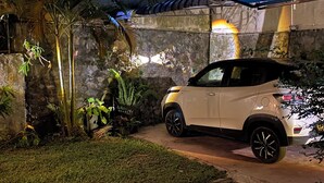A white SUV parked under a blue canopy in a garden with stone walls and tropical plants.