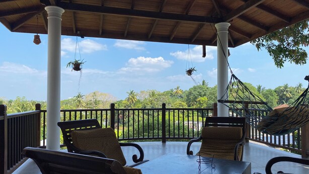 A covered outdoor seating area with a table and chairs, a hammock, and hanging planters.