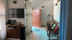 A living room with a TV, wooden furniture, a trash bin, and a door leading to another room.