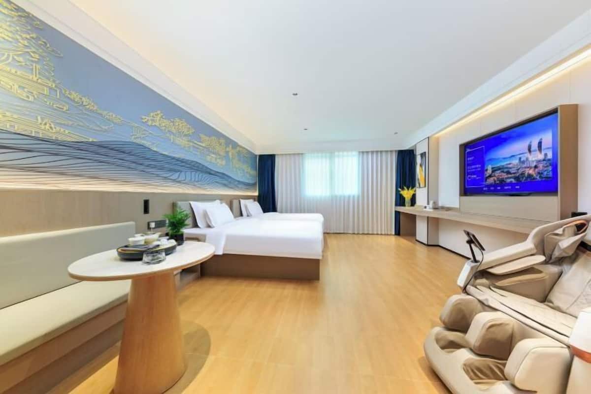 Een moderne hotelkamer met een bed, een zithoek, een massagestoel, een televisie en een muurschildering.