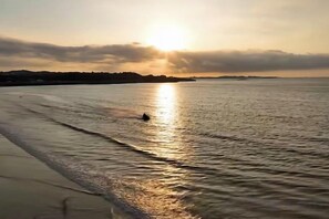 Eine Strandansicht mit der Sonne, die sich im Wasser spiegelt, einem wolkenlosen Himmel und einer fernen Küste.