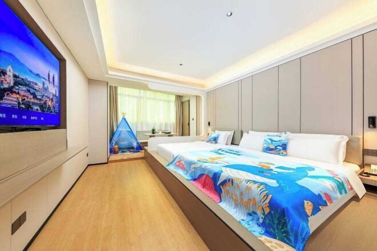 Een moderne hotelkamer met een groot bed, een flatscreen televisie aan de muur en uitzicht op de stad.