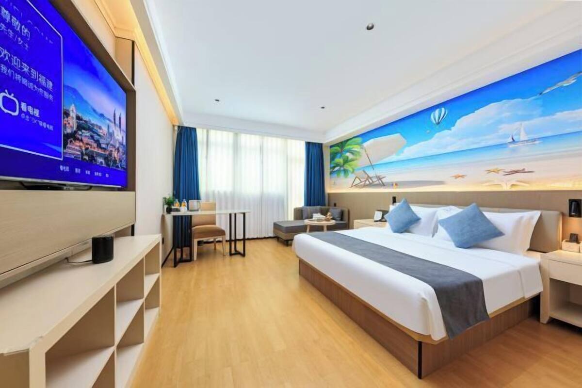 Een hotelkamer met een groot bed, een televisie, een bureau en een schilderij van een strand.