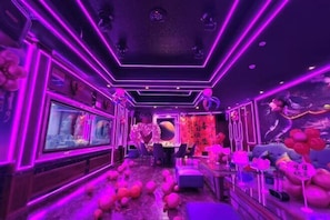 A room with a long, narrow layout, a large flat-screen TV, and a bar area with stools.