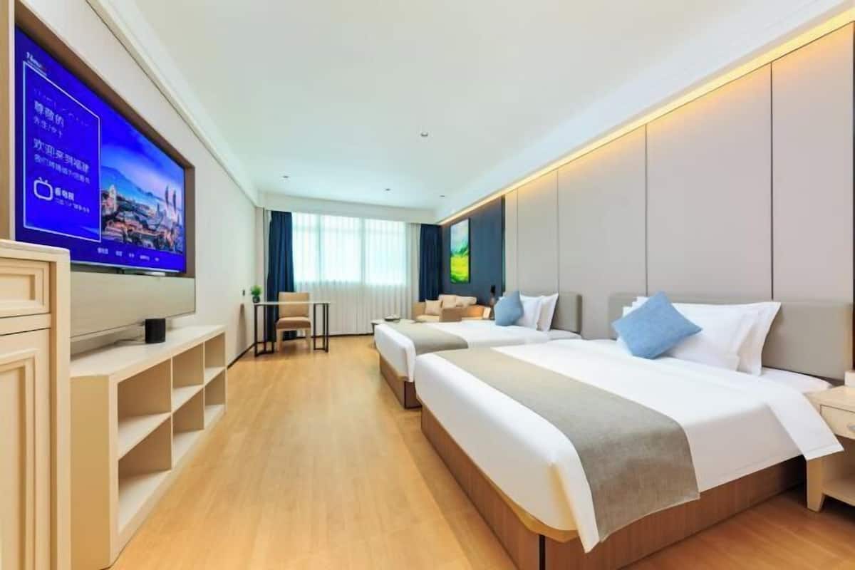 Een hotelkamer met een grote flatscreen televisie, twee bedden, een bureau en een stoel.