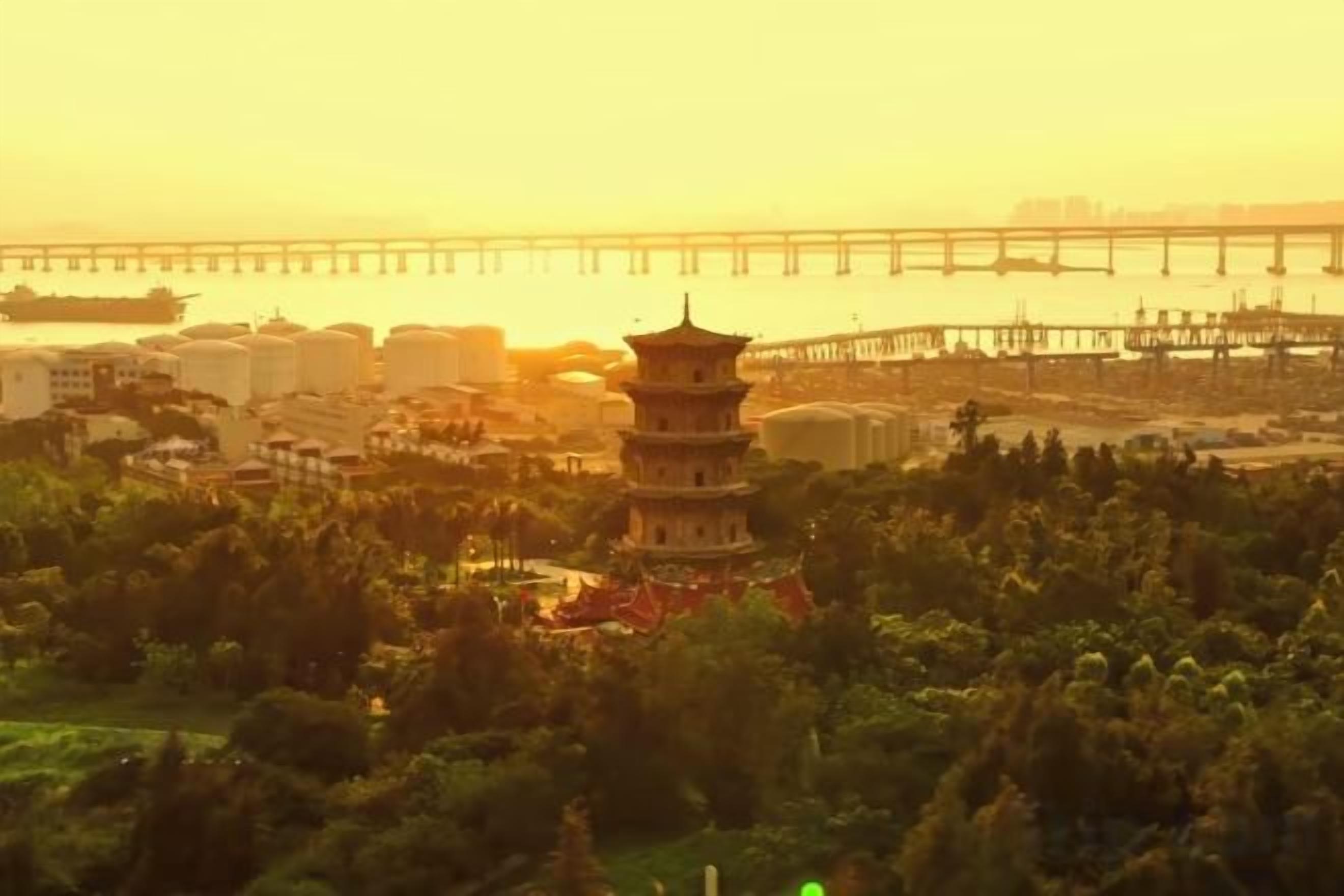 A pagoda surrounded by greenery, a bridge, and industrial buildings in the background.