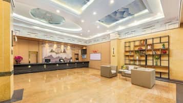 A hotel lobby with a reception desk, seating area, and a wall with shelves.