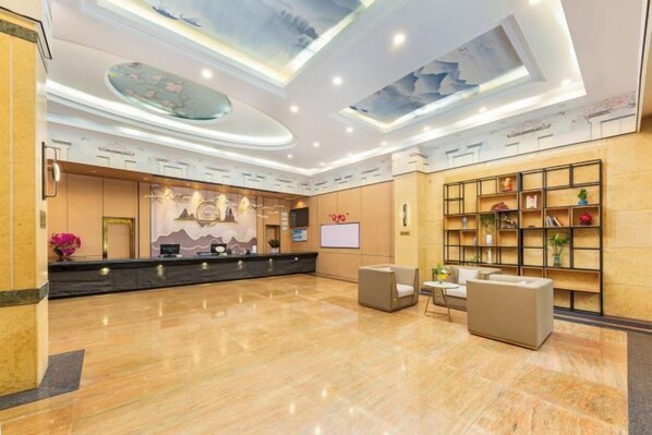 A hotel lobby with a reception desk, seating area, and a wall with shelves. - Xiangjiang Hotel Shishi (Shishi)