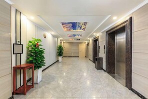 Eine Hotelhalle mit Marmorboden, einer Rezeption, Topfpflanzen, einer Uhr und einem Aufzug.