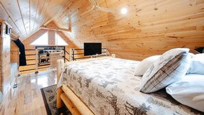 A cozy wooden cabin room with a bed, a television, and a window overlooking a scenic view. - Cozy 2BR 2Bath Cabin, minutes from OU, Hocking Hills, Zaleski Forest. (Albany)