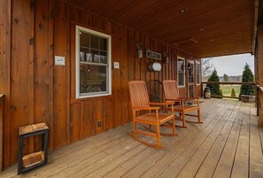 Une véranda en bois avec des fauteuils à bascule, une pancarte de bienvenue et une vue sur le paysage environnant.