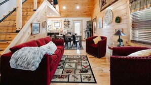 A wooden cabin interior with a staircase, red sofas, a dining area, and a kitchen. - Cozy 2BR 2Bath Cabin, minutes from OU, Hocking Hills, Zaleski Forest. (Albany)