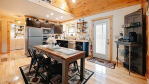 A modern kitchen with wooden ceiling beams, a dining area with a table and chairs, and a coffee station. - Cozy 2BR 2Bath Cabin, minutes from OU, Hocking Hills, Zaleski Forest. (Albany)